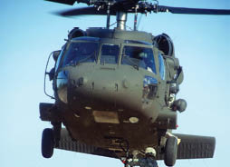 Military helicopter flying against a clear blue sky, showcasing its rotor blades, dark green exterior, and detailed cockpit.